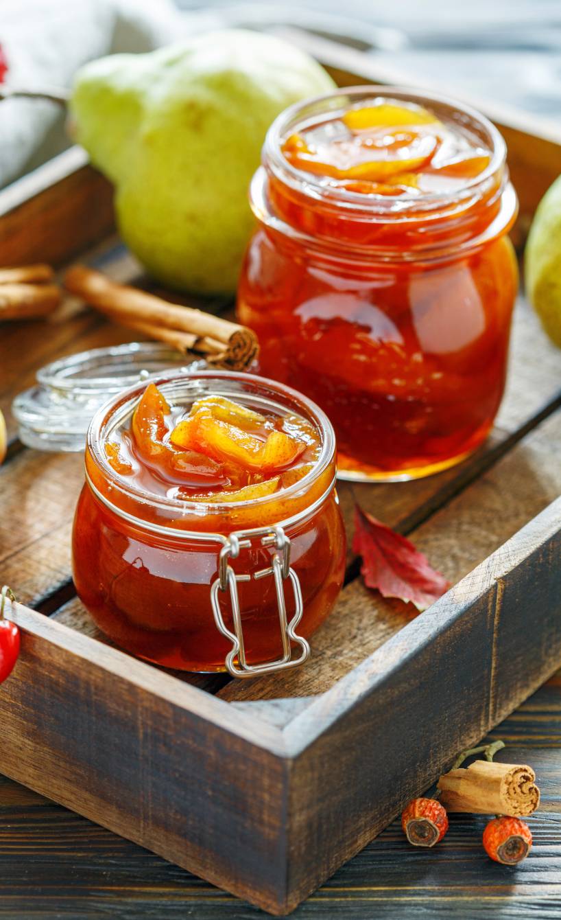 Selbst gekochte Birnenkonfitüre in zwei Weckgläsern auf einem Holztablett, daneben Zimtstangen auf einem Tisch