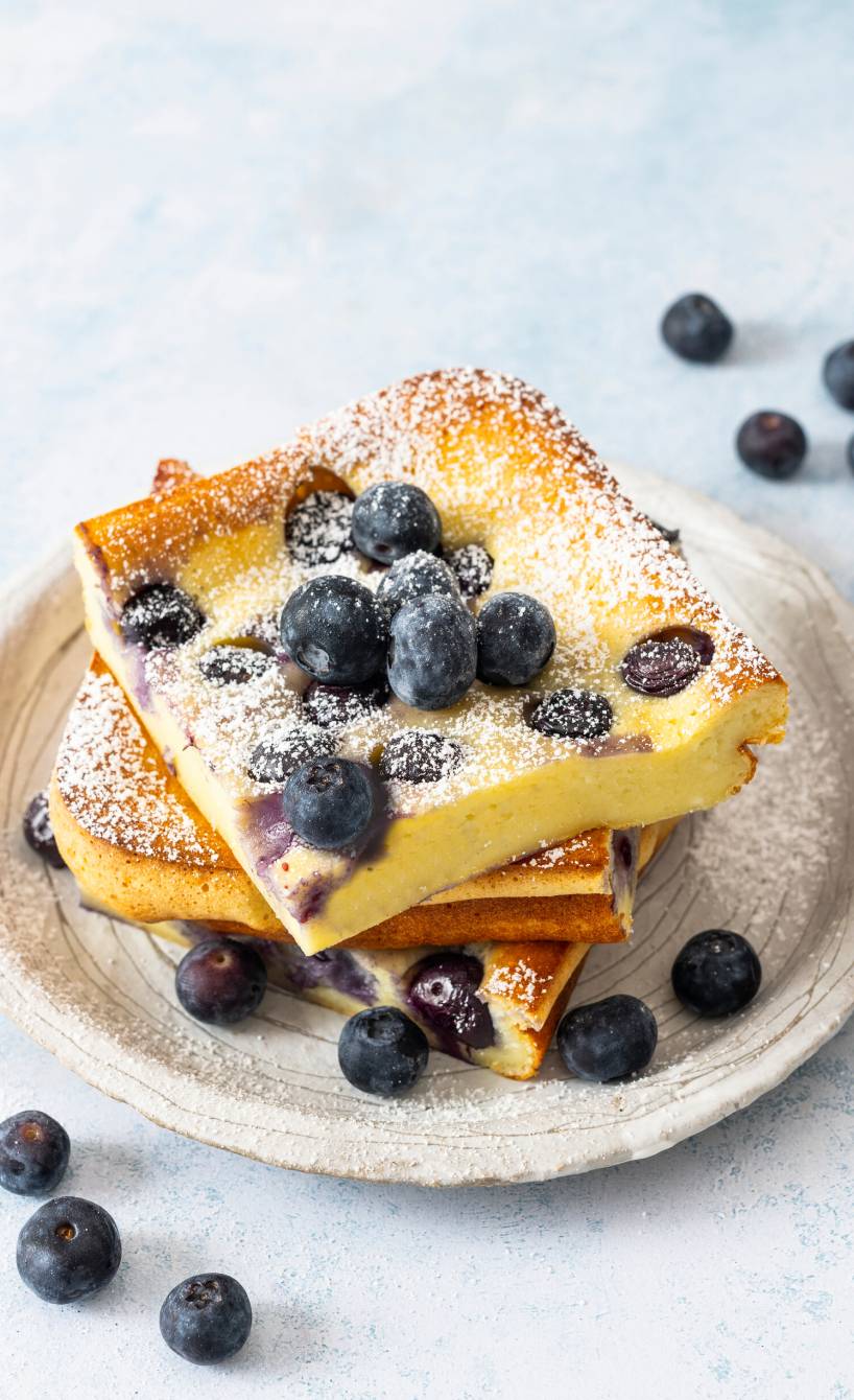 Mehrere Stücke Ofenpfannkuchen mit Blaubeeren gestapelt auf einem Kuchenteller betäubt mit Puderzucker