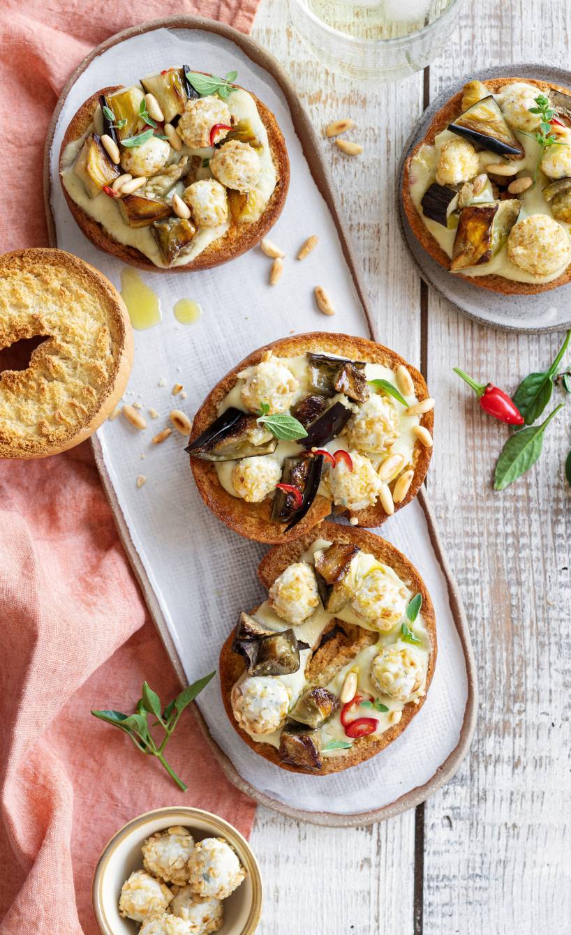 Mehrere Brotringe bestrichen mit Auberginencreme und getoppt von Pinienkern-Käsebällchen auf einer Servierplatte