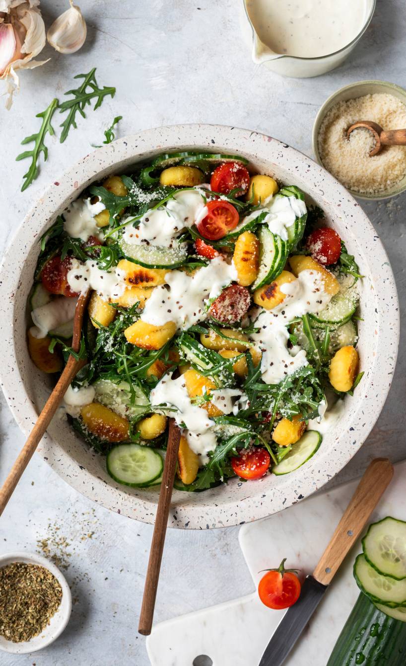 Gurkensalat mit gebratenen Gnocchi in einer Salatschüssel, daneben Zutaten und Parmesan