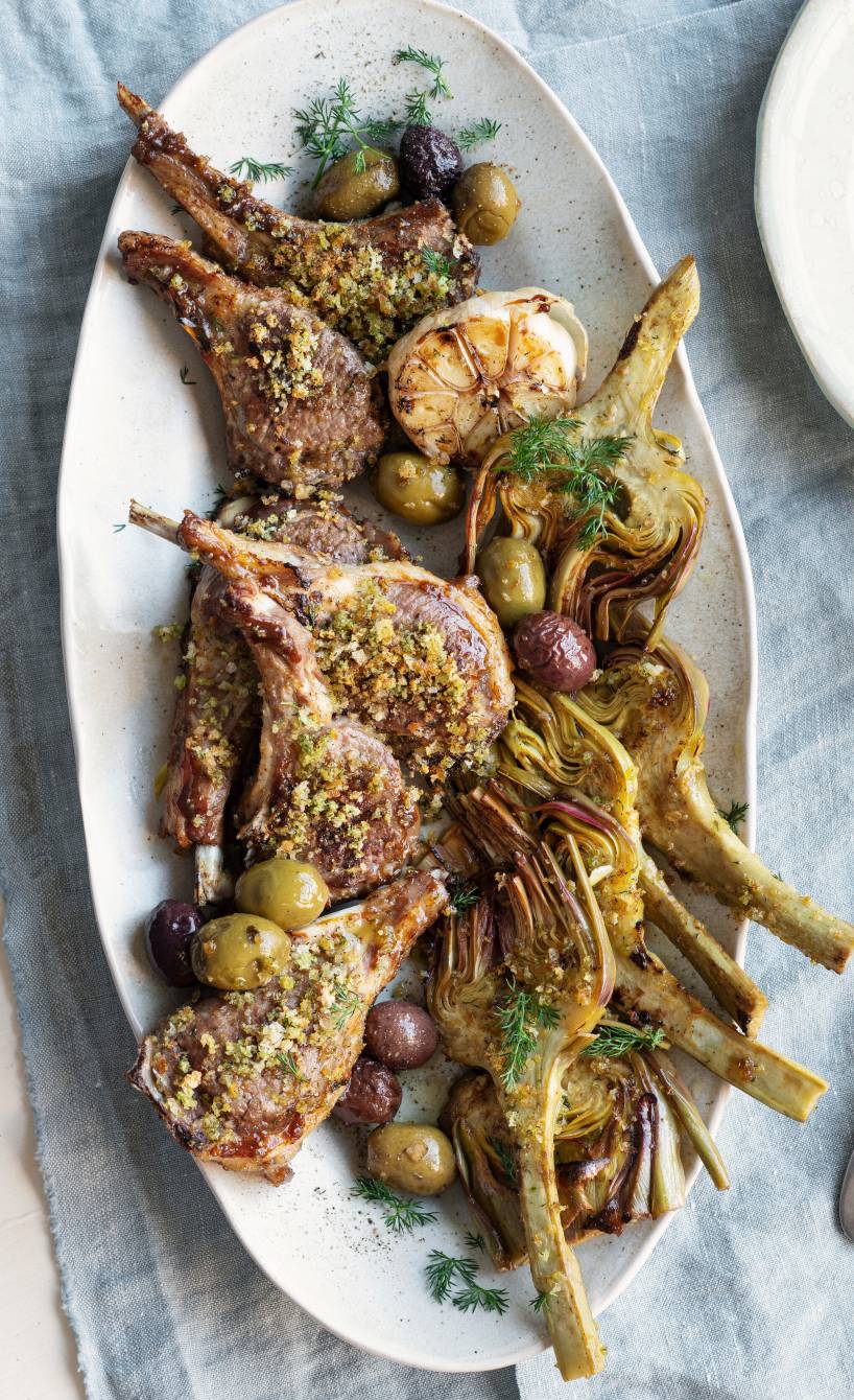 Mehrere gebackene, gratinierte Lammkotelett mit Artischocken, Oliven und Knoblauch angerichtet auf einer Servierplatte