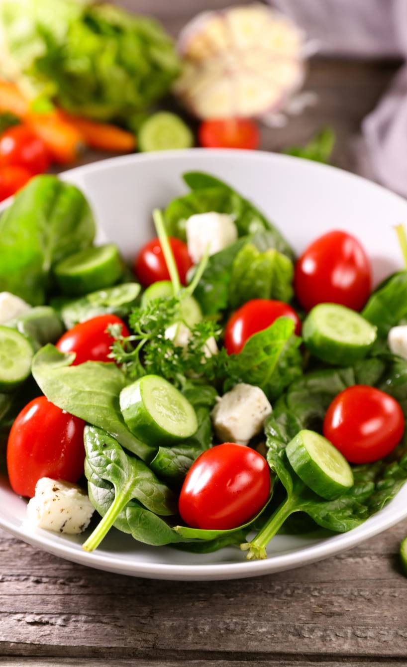 Gurkensalat mit Tomaten auf einem Teller, daneben viele weitere Zutaten auf einem Tisch