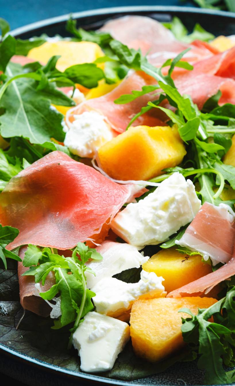 Melonensalat mit Rucola, Prosciutto und Mozzarella in einem tiefen Teller in Nahaufnahme auf einem Tisch