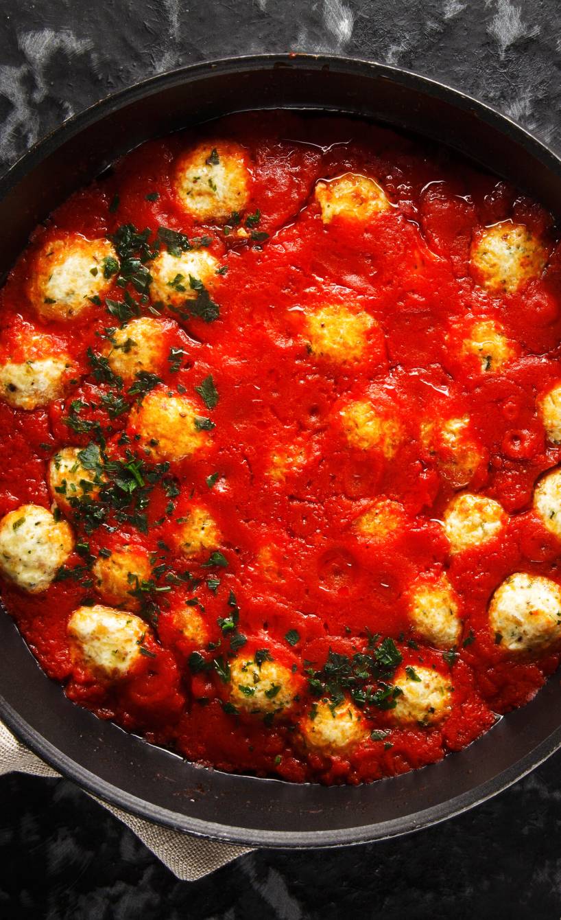 Ricotta-Bällchen in Tomatensoße in einem Topf getoppt mit Basilikum auf einem Esstisch