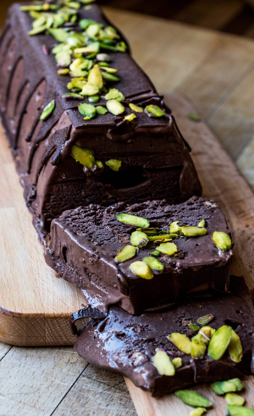 Dunkles Schokoladen-Semifreddo aus der Kastenform mit Pistazien getoppt angeschnitten auf einem Holzbrett