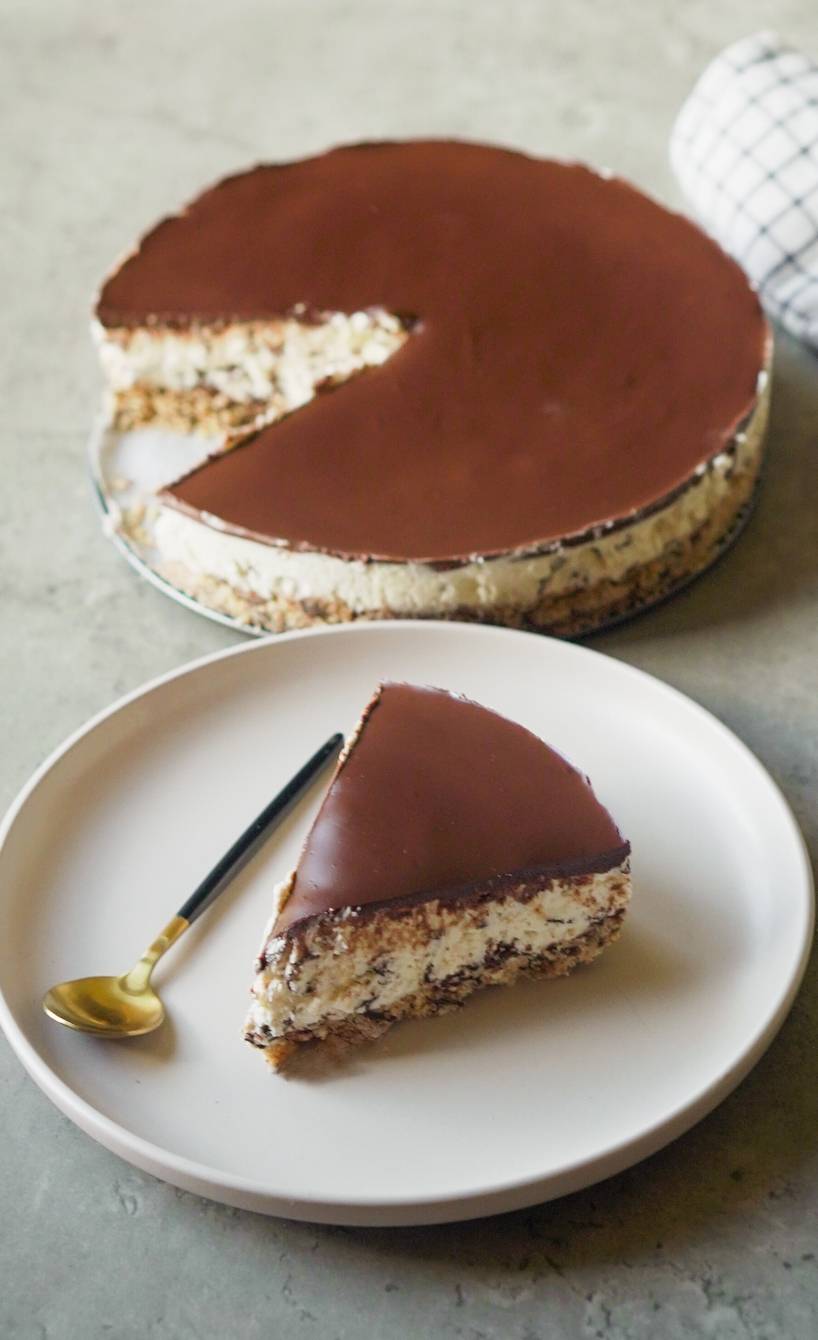 Stracciatella Torte ohne Backen angeschnitten auf einer Kuchenplatte, davor ein Stück auf einem Kuchenteller