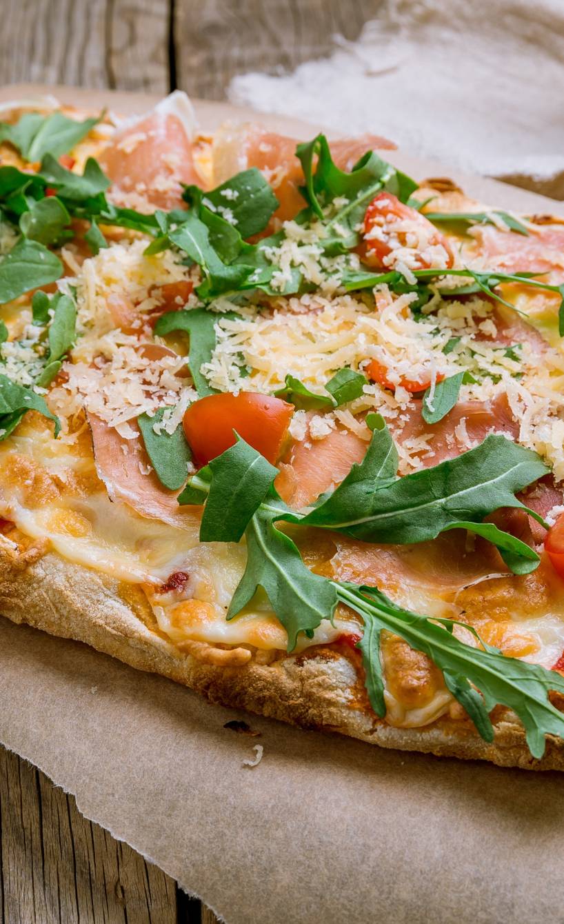 Ovale Pinsa mit knusprigem Boden und buntem Belag auf einem Holzbrett