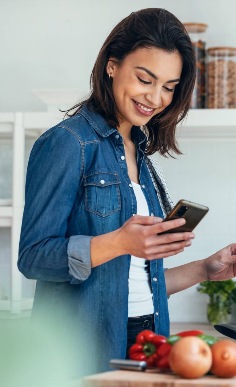 Eine Frau steht in ihrer Küche und kocht, während sie sich das Rezept auf dem Handy anschaut
