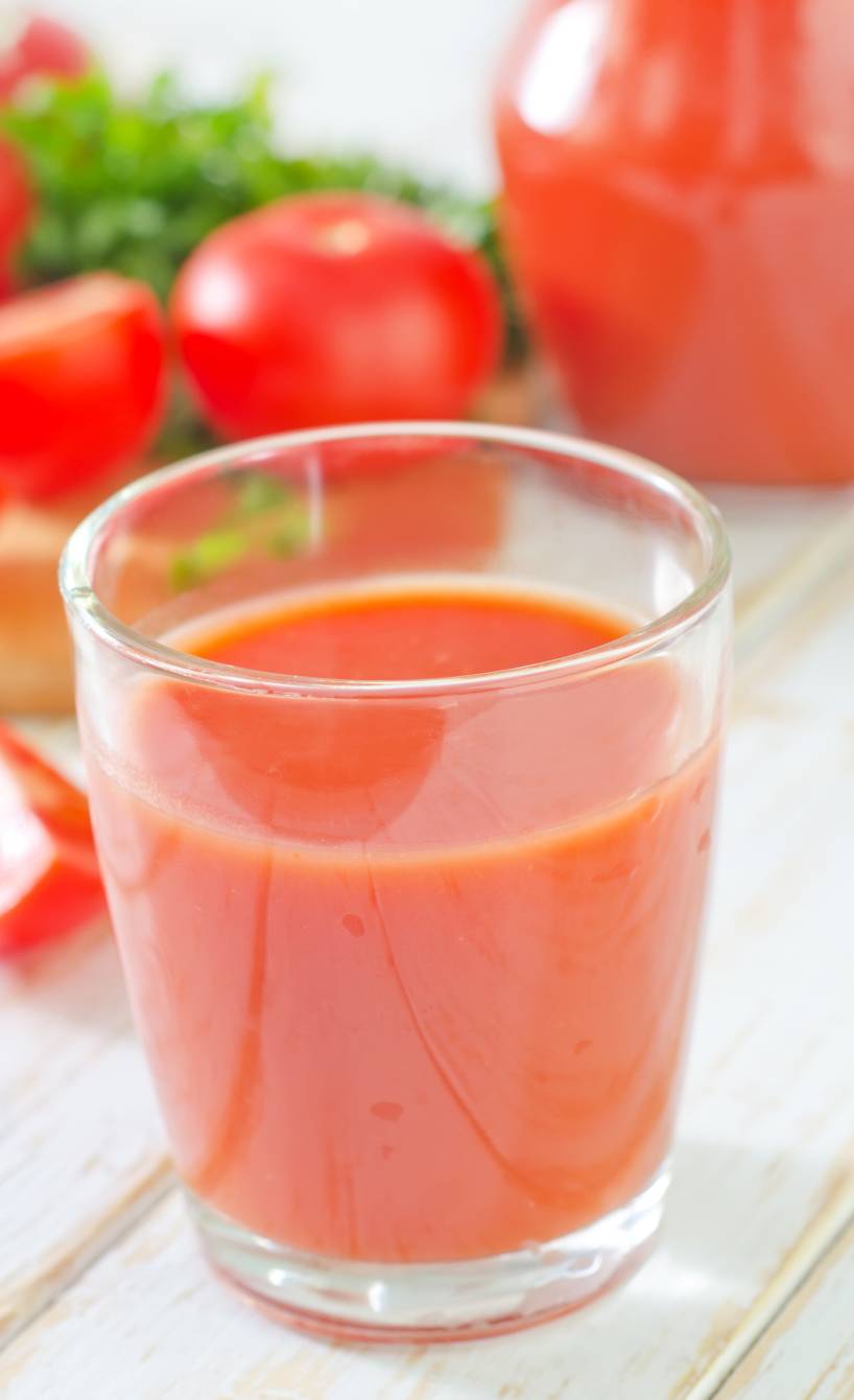 Ein Glas Tomatensaft selbst gemachter Tomatensaft vor einer Karaffe auf einem Holztisch, daneben frische Tomaten