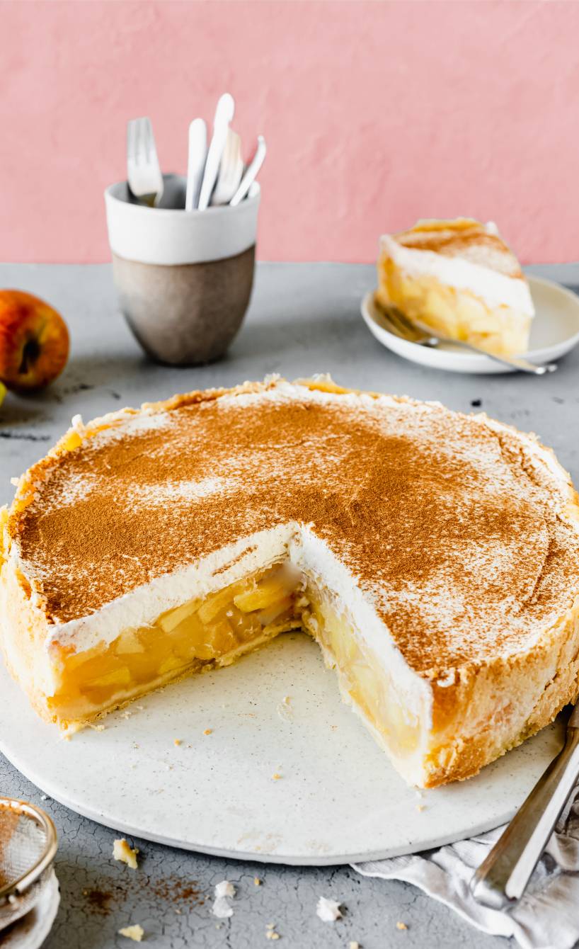 Runde Apfel-Wein-Torte mit Vanillesahne angeschnitten auf einer Tortenplatte bestäubt mit Zimt