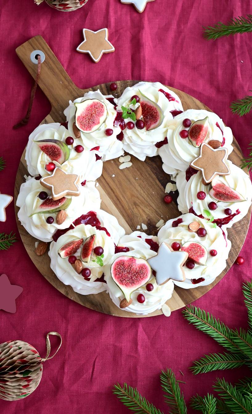 Weihnachts-Baiserkranz mit Mascarponecreme getoppt von Cranberry-Kompott, dekoriert mit frischen Feigen, Mandeln und Lebkuchensternen auf einem Holzbrett