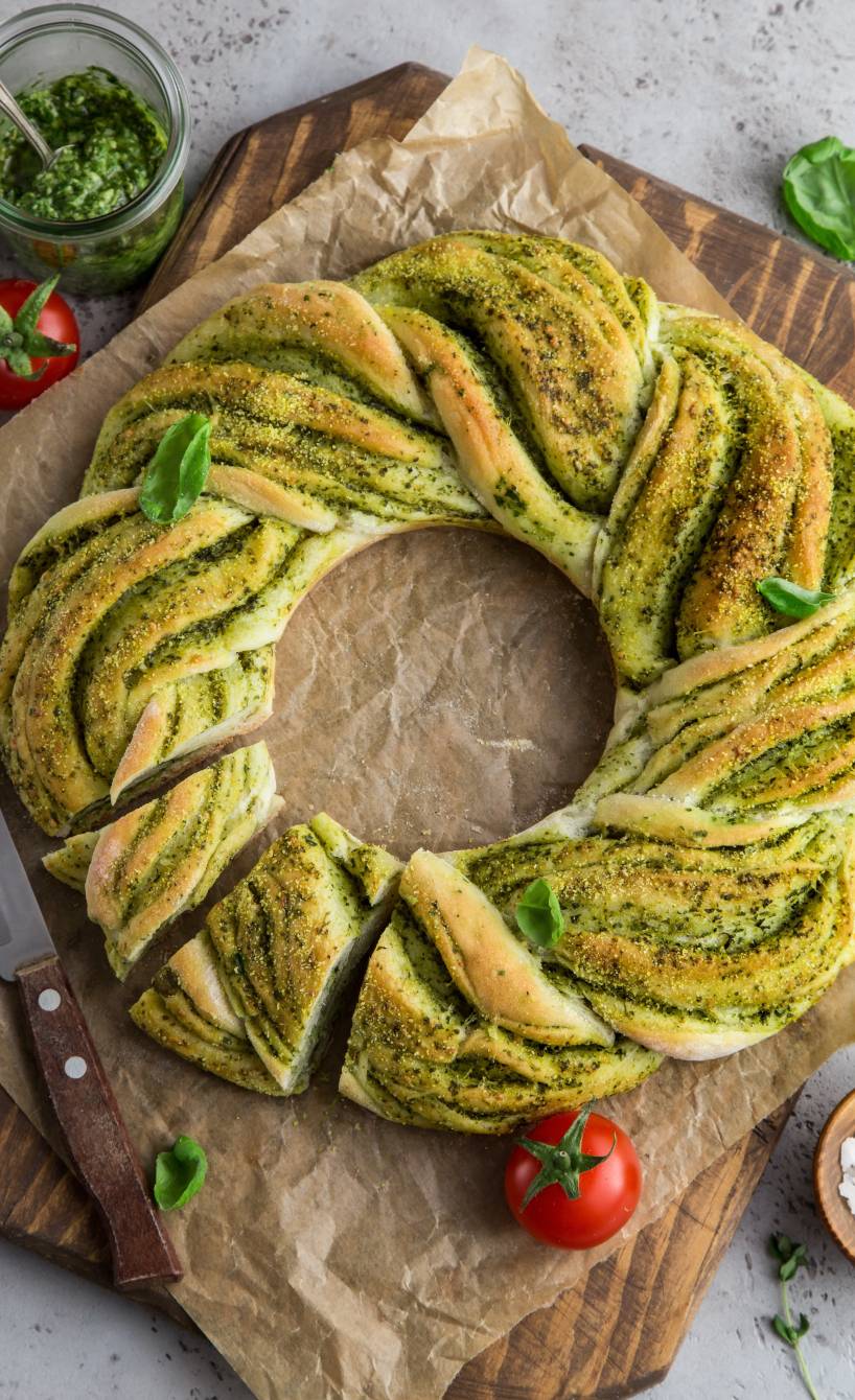 Selbst gebackener Brotkranz mit grünem Basilikum-Pesto angeschnitten auf einem Holzbrett
