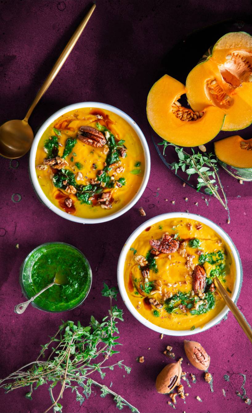 Selbstgekochte Kürbis-Ingwer-Suppe angerichtet in zwei Suppentellern getoppt von Kräuteröl und Nüssen
