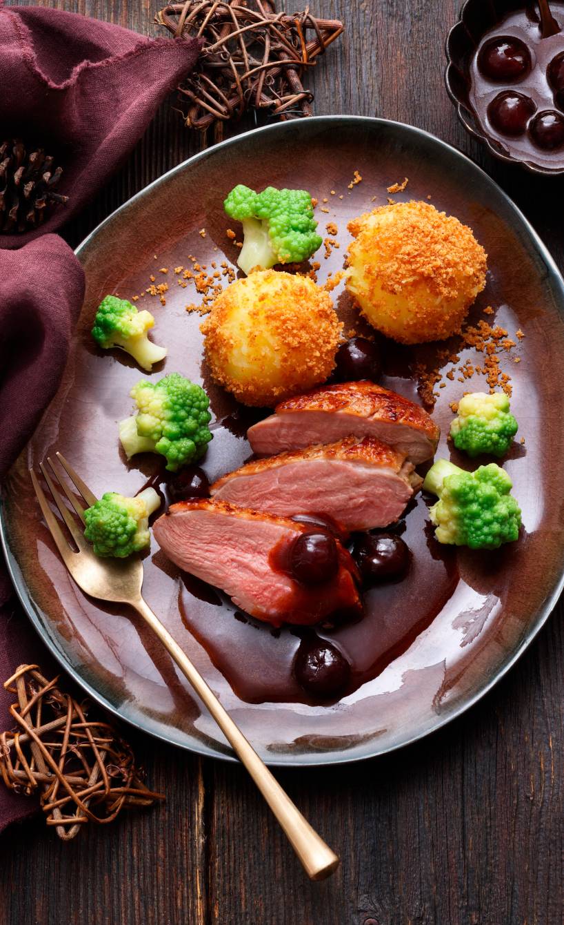 Entenbrustfiletstücke festlich angerichtet auf einem Teller mit Romanesco und panierten Klößen übergossen mit Amarenasoße