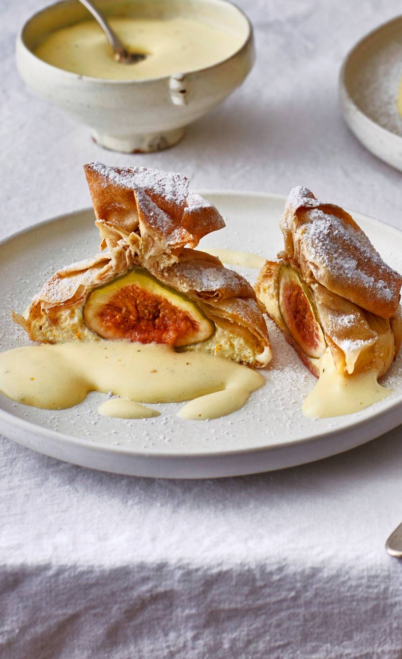 Halbiertes Filoteig-Päckchen gefüllt mit ganzen Feigen und Ricotta auf einem Bett aus Limetten-Zabaione auf einem Dessertteller