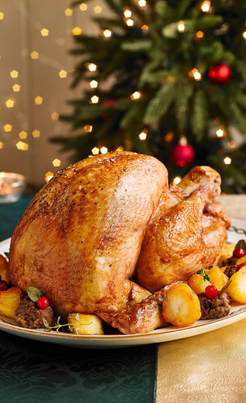 Ganze gefüllte Poularde auf einer Servierplatte umgeben von Hackbällchen, Kartoffeln und Früchten