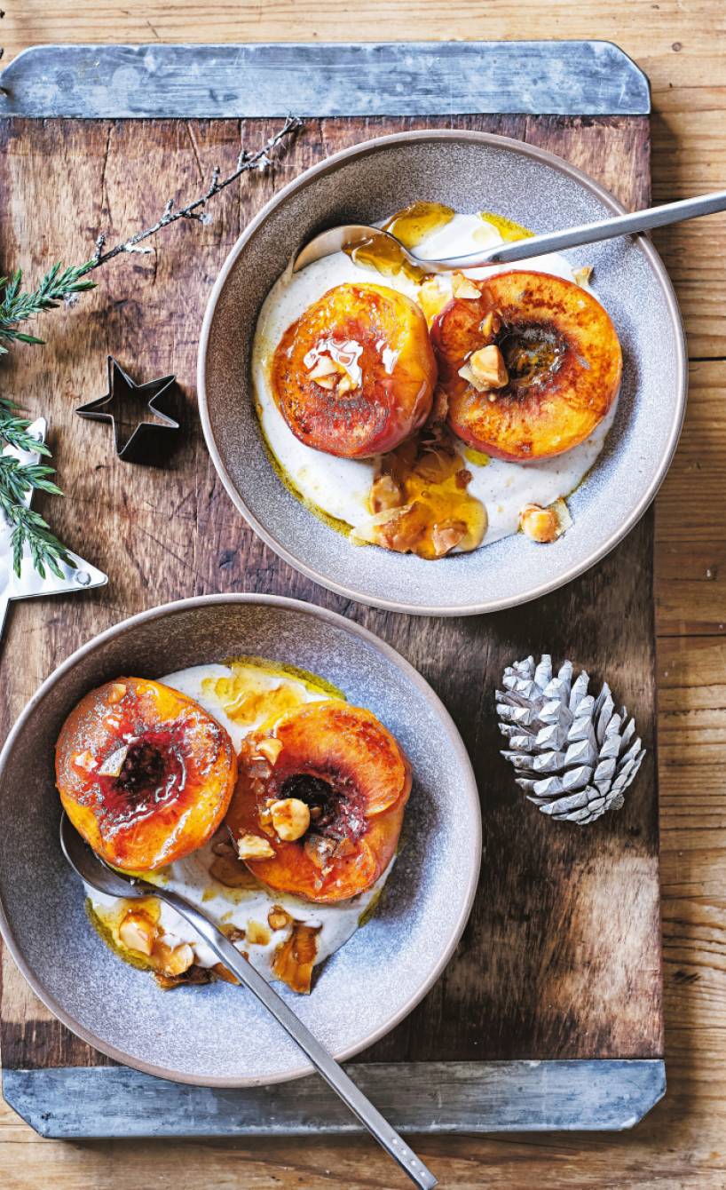 Zwei Portionen veganes Weihnachtsdessert aus gebratenen Pfirsichen auf Zimtjoghurt mit Nusstopping in zwei Dessertschalen