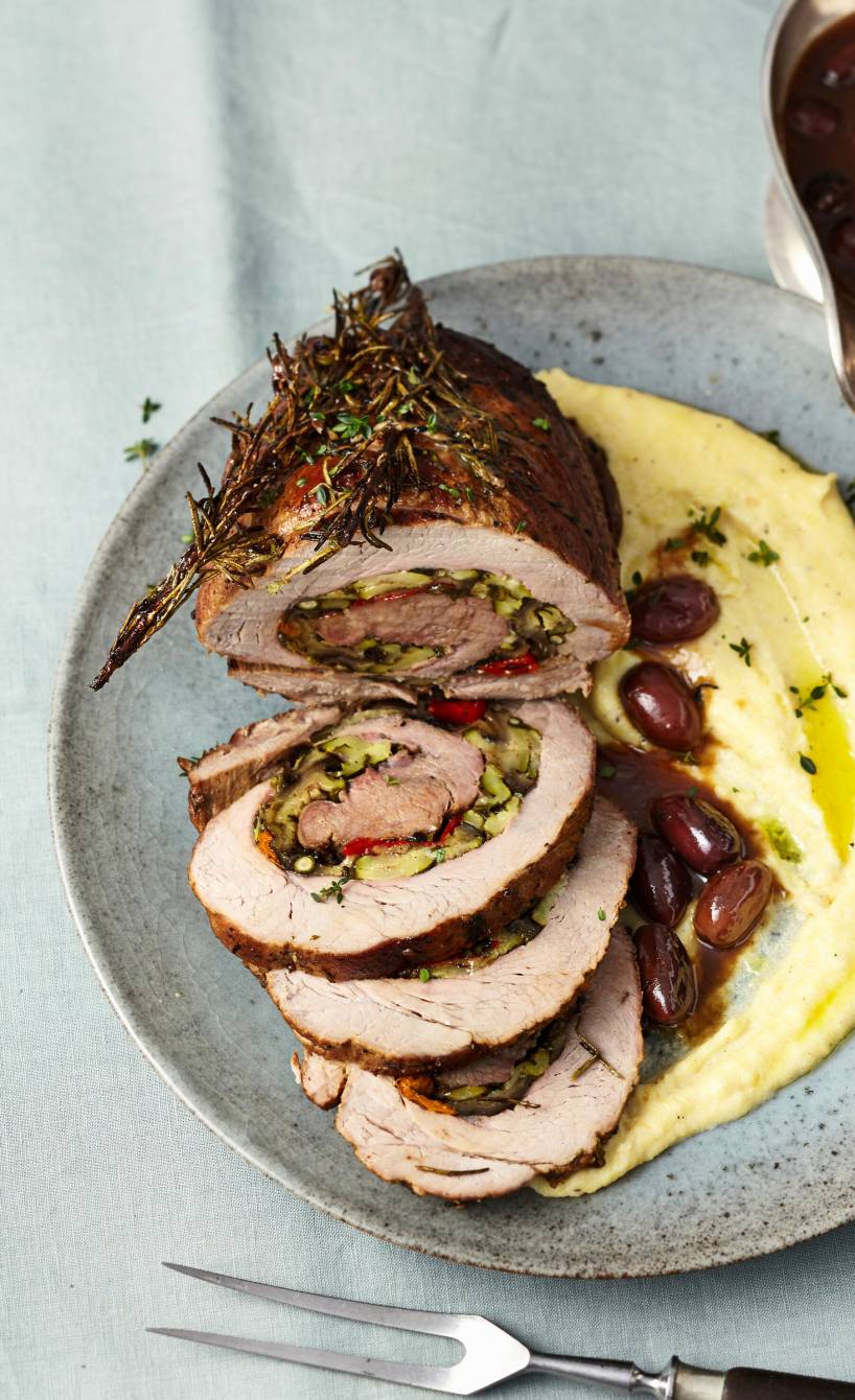 Rollbraten mit mediterraner Gemüsefüllung angeschnitten auf einer Servierplatte, daneben Polenta