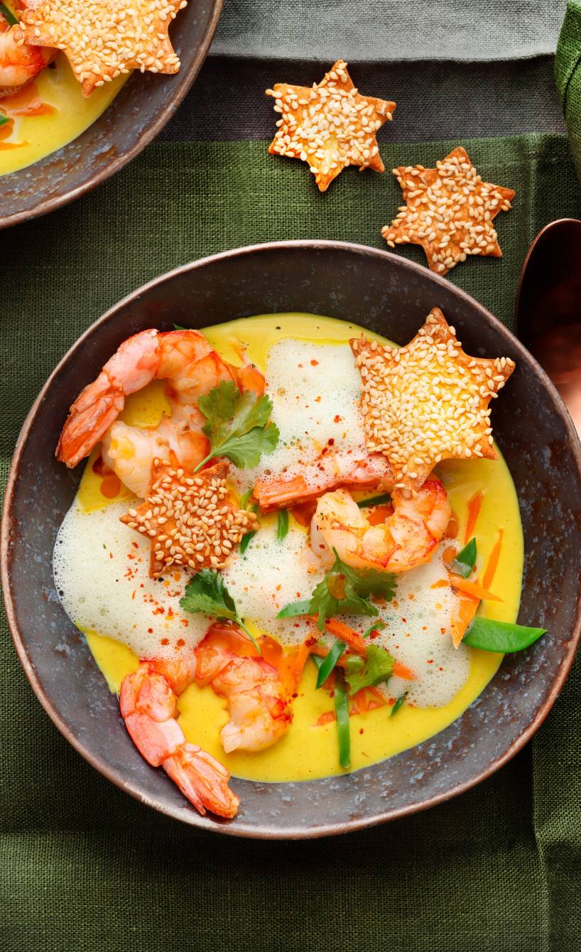 Karottencremesuppe in mehreren Suppentellern getoppt von gebratenen Garnelen, Wan Tan-Knuspersternen und Milchschaum auf einem weihnachtlich dekorierten Tisch