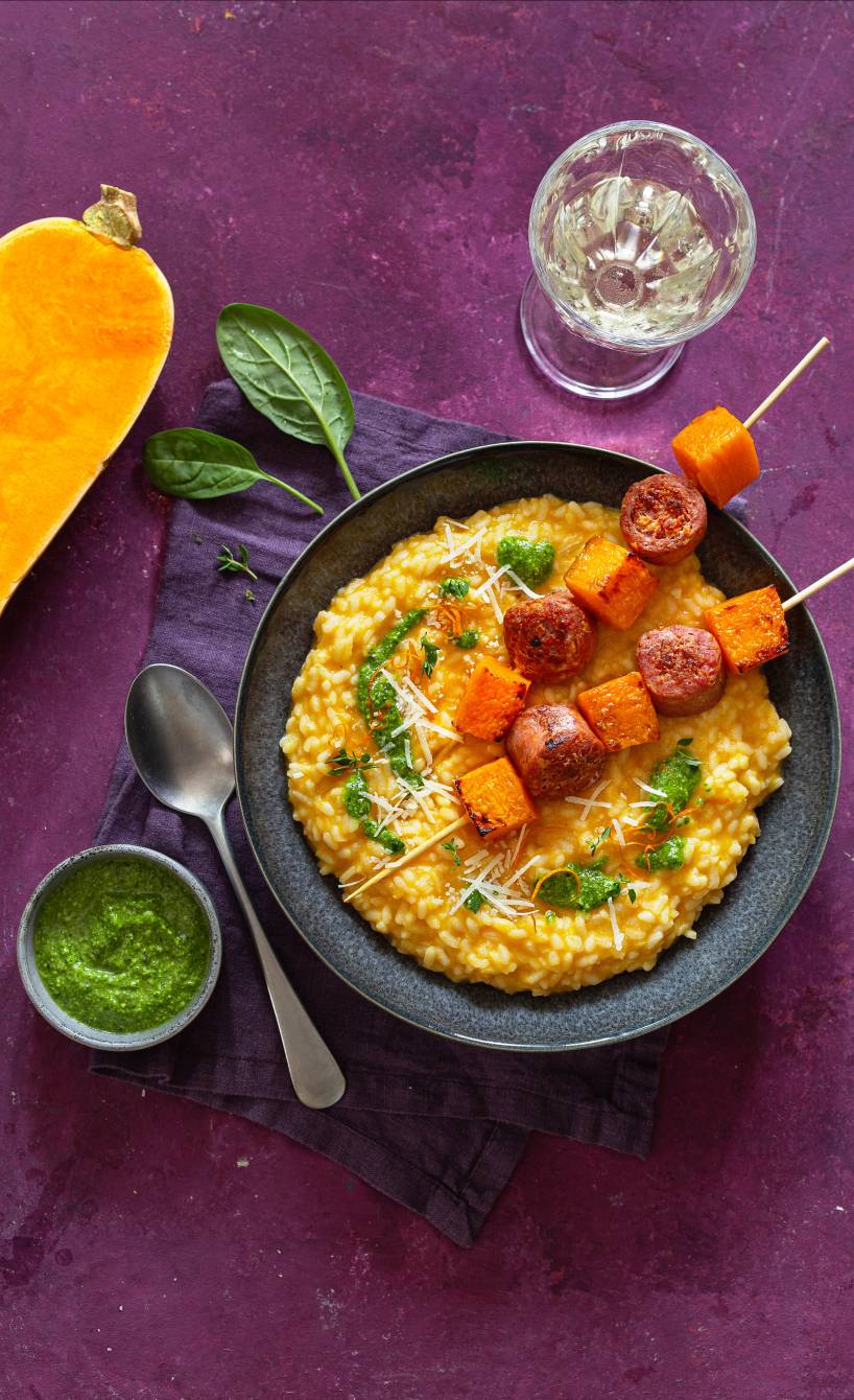 Butternutkürbis-Risotto getoppt mit Salsiccia-Spießen auf einem Tisch