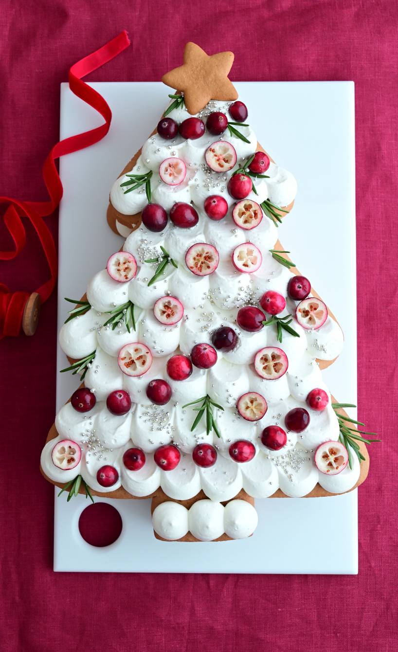 Weihnachtsbaum aus Honigkuchen mit weißem Frosting und Deko auf einer Tortenplatte