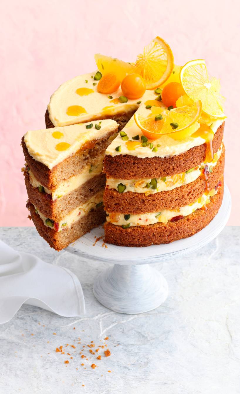 Italienische Lebkuchen-Weihnachtstorte mit Orangencreme und Pistazien angeschnitten auf einer Tortenplatte dekoriert mit Physalis und Orangenscheiben