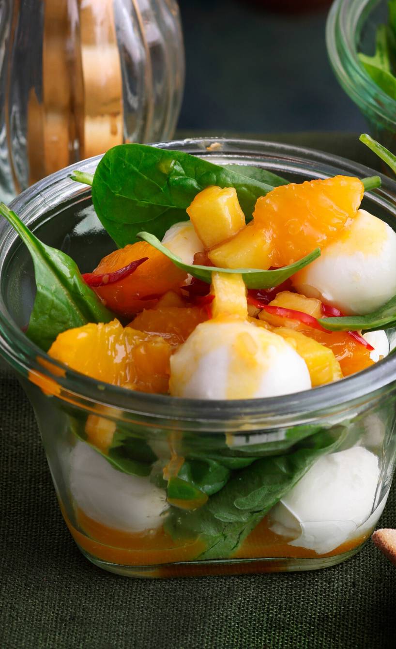 Mehrere Gläser mit Mozzarella auf Blattspinat und Orangen-Chutney auf einem Tisch, daneben Grissini