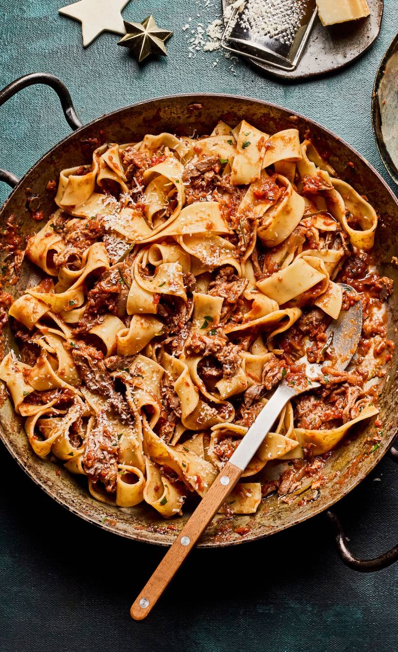 Pappardelle mit Enten-Ragù in einer tiefen Pfanne auf einem festlich dekorierten Tisch, daneben Parmesan