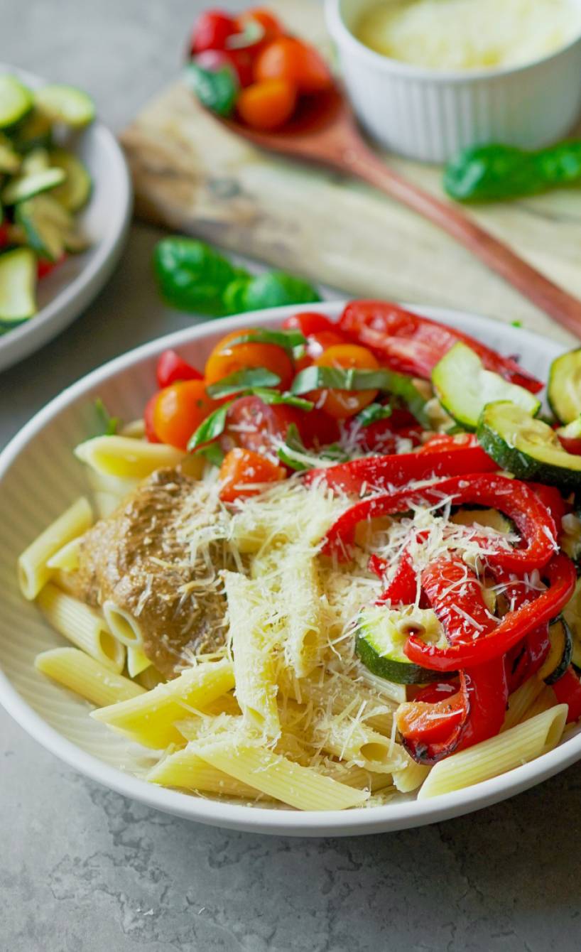 Pasta-Bowl mit Ofengemüse auf einem tiefen Teller, daneben geriebener Parmesan