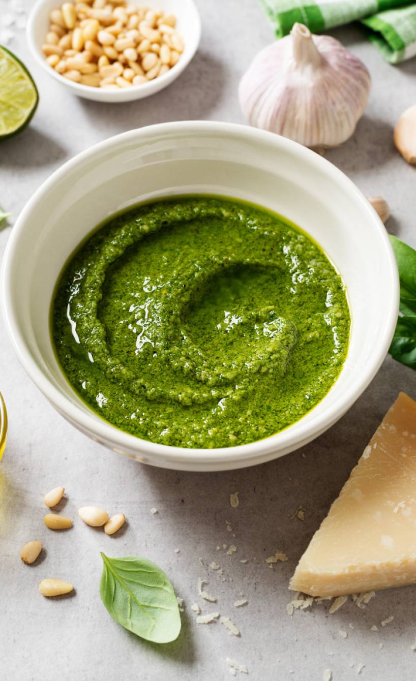 Selbstgemachtes Basilikumpesto alle Genovese in einer Schale, drumherum einige Zutaten wie Olivenöl, Pinienkerne und Käse