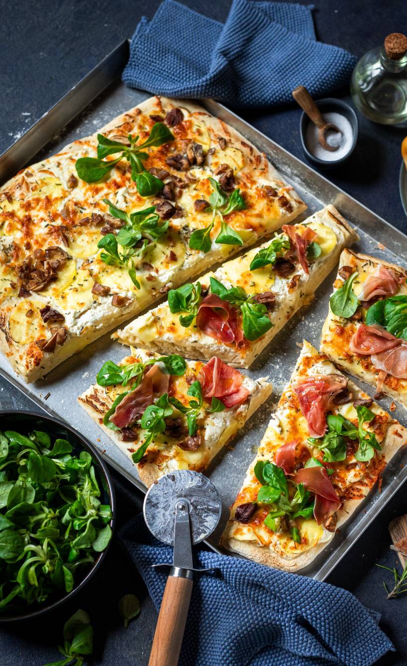 Weiße Pizza Bianca belegt mit Kartoffeln, Maronen, Feldsalat und Parmaschinken angeschnitten auf einem Backblech