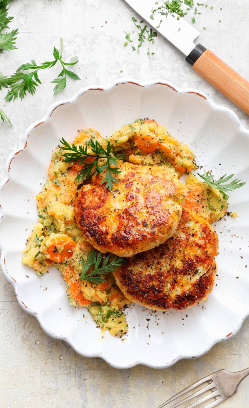 Zwei gebratene Putenfrikadellen mit Quark und Haferflocken auf einem Teller mit Karottenpolenta