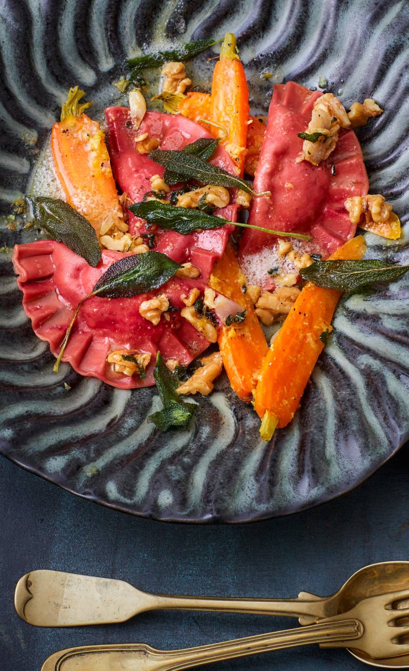 Selbst gemachte Rote Bete-Ravioli mit Käsefüllung angerichtet auf einem Teller mit Ingwer-Karotten und Walnusstopping