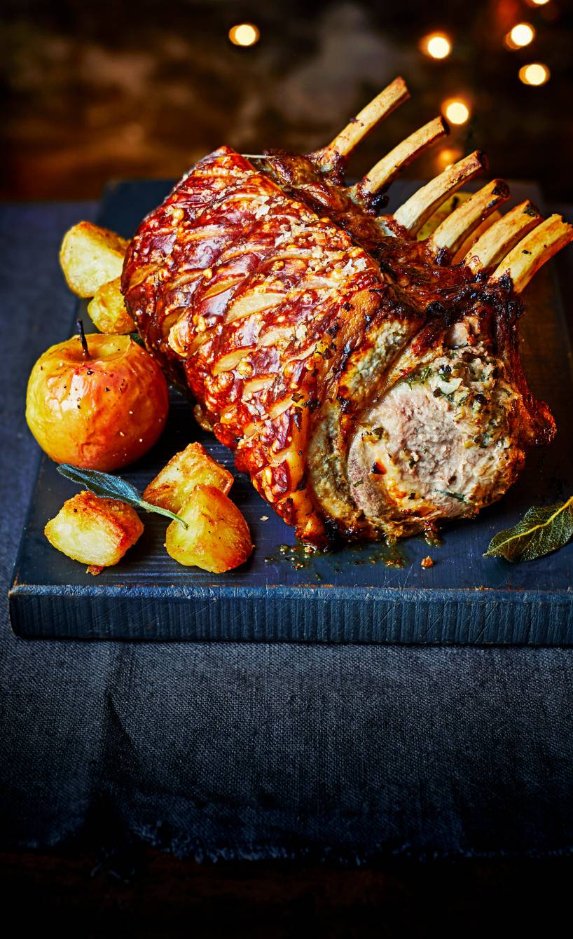 Schweinekotelette-Braten mit Semmelknödel-Füllung angerichtet auf einer Servierplatte, daneben Bratäpfel und Kartoffeln