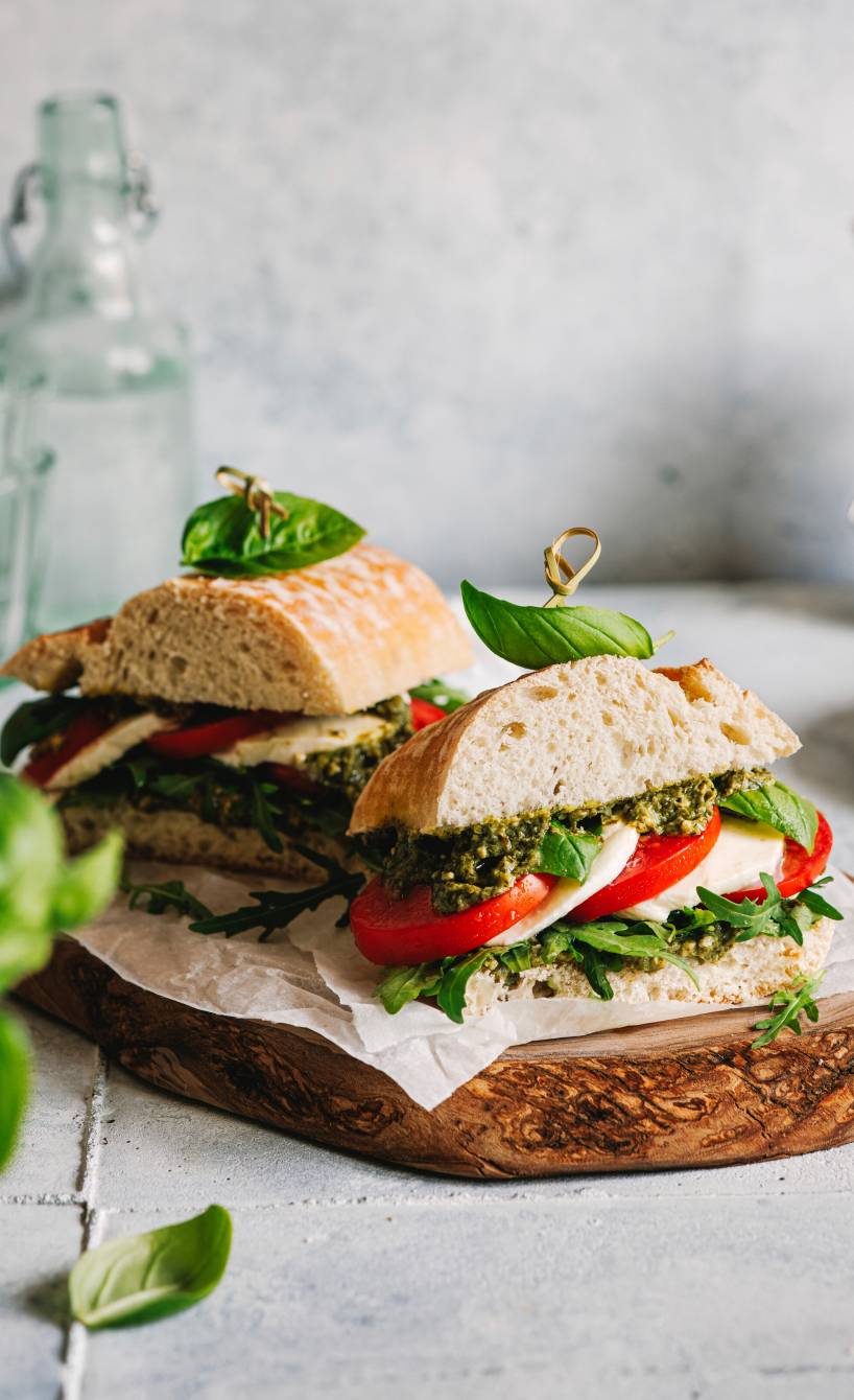 Zwei Panini-Brot belegt mit Tomate, Mozzarella und Basilikumpesto angerichtet auf einem Holzbrett
