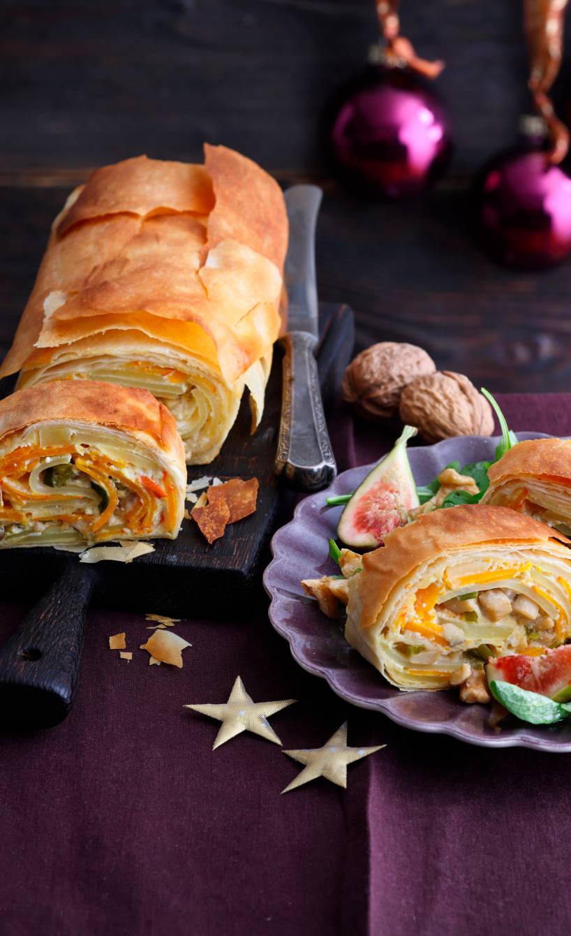 Veganer Kürbisstrudel gefüllt mit Pilzen und Kartoffeln angeschnitten auf einer Platte, davor ein Stück auf einem Teller