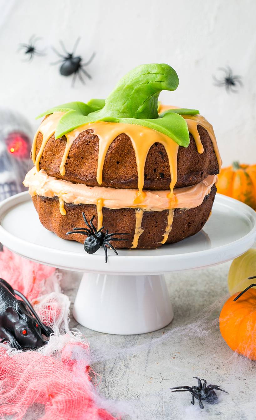 Kuchen, der aussieht wie ein Kürbis auf einer Kuchenplatte auf einem für Halloween dekorierten Tisch