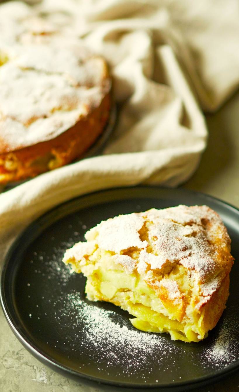 Ein Stück italienischer Apfelkuchen nach Torta die Mele Rezept auf einem Kuchenteller, dahinter der Rest des Kuchens