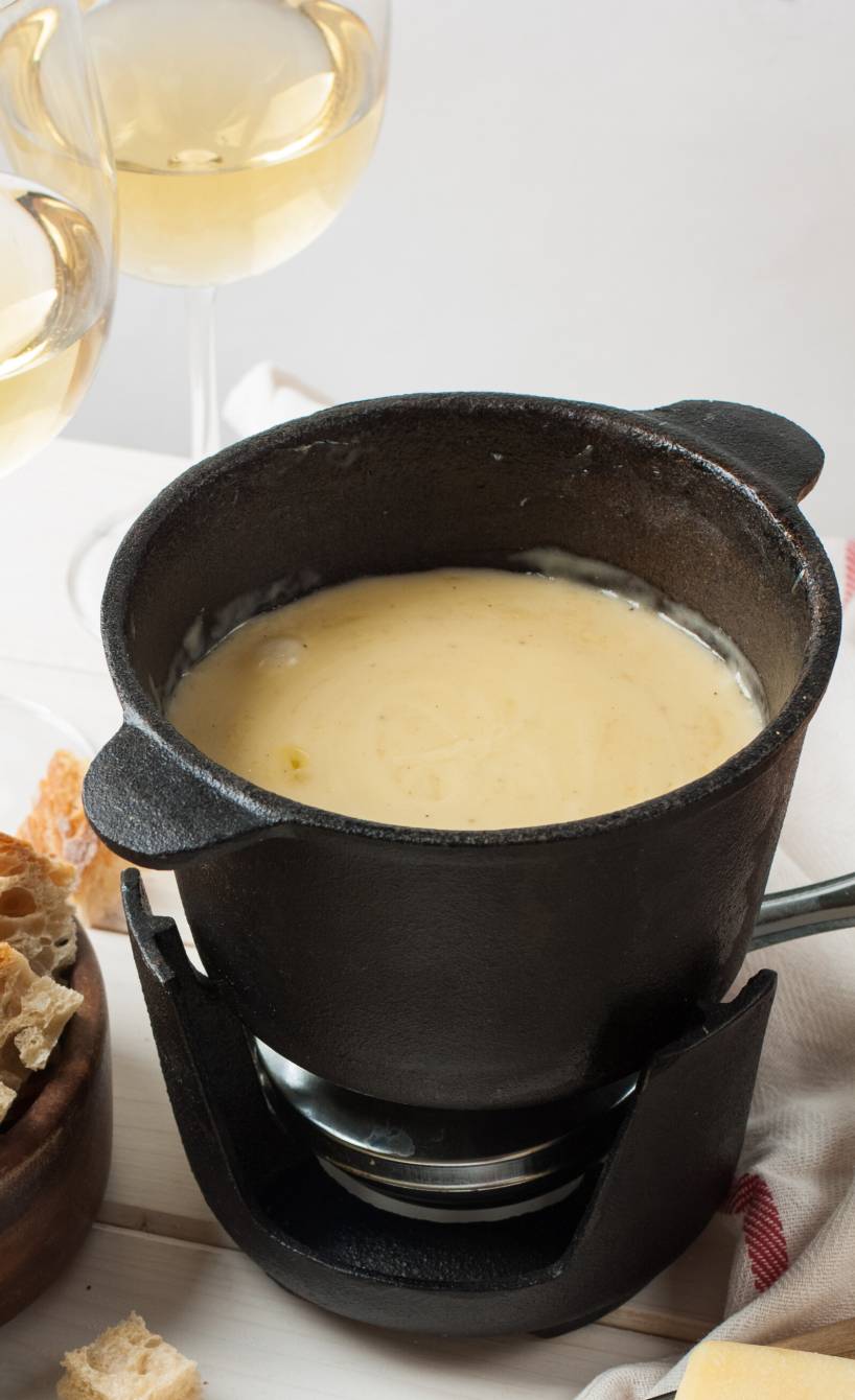 Fonduta, italienisches Käsefondue, in einem Fonduetopf, daneben Käse und Trauben auf einem Tisch