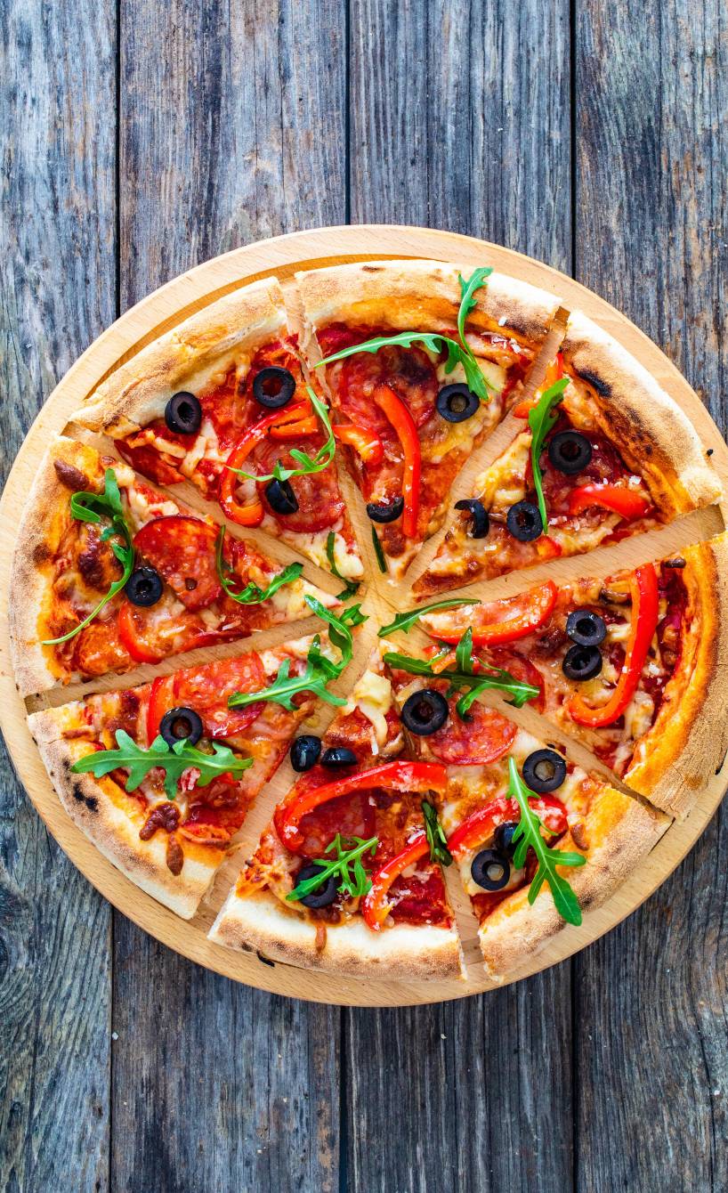 Runde Pizza in Pizzastücke geschnitten mit Nduja-Salami, Oliven, Mozzarella und Rucola belegt auf einem Tisch