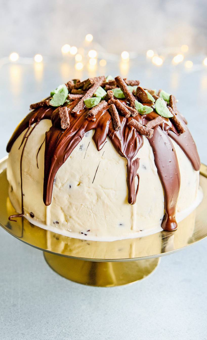 Selbstgemachte Minz-Schoko-Eisbombe auf einer Servierplatte garniert mit Schokolade und grüner Minzschokolade
