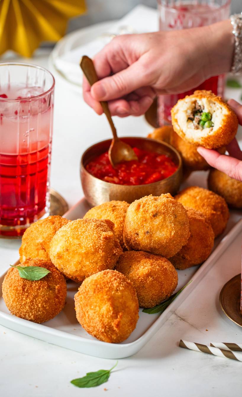 Arancini mit Hackfleisch-Erbsenfüllung auf einem Buffet, daneben Tomatensalsa
