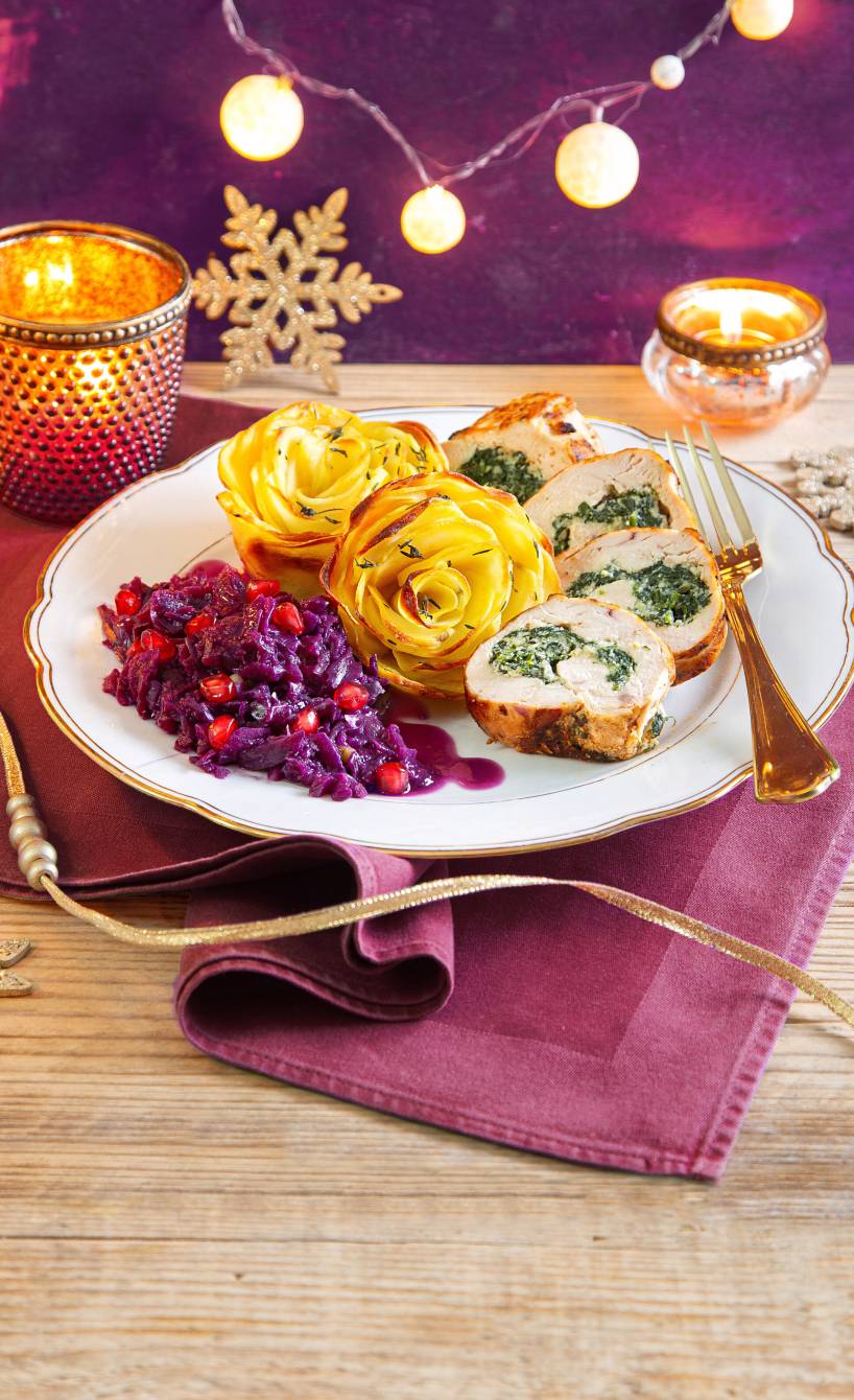Gefüllte Hähnchenbrust mit Ricotta-Spinat-Füllung angerichtet mit Kartoffelrosen und Granatapfel-Rotkohl auf einem Teller