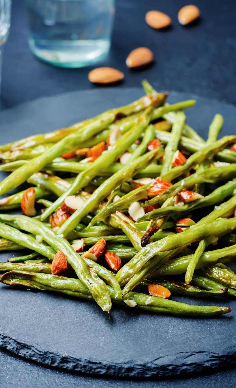 Gebratene grüne Bohnen bestreut mit Mandelkernen auf einem Schieferteller