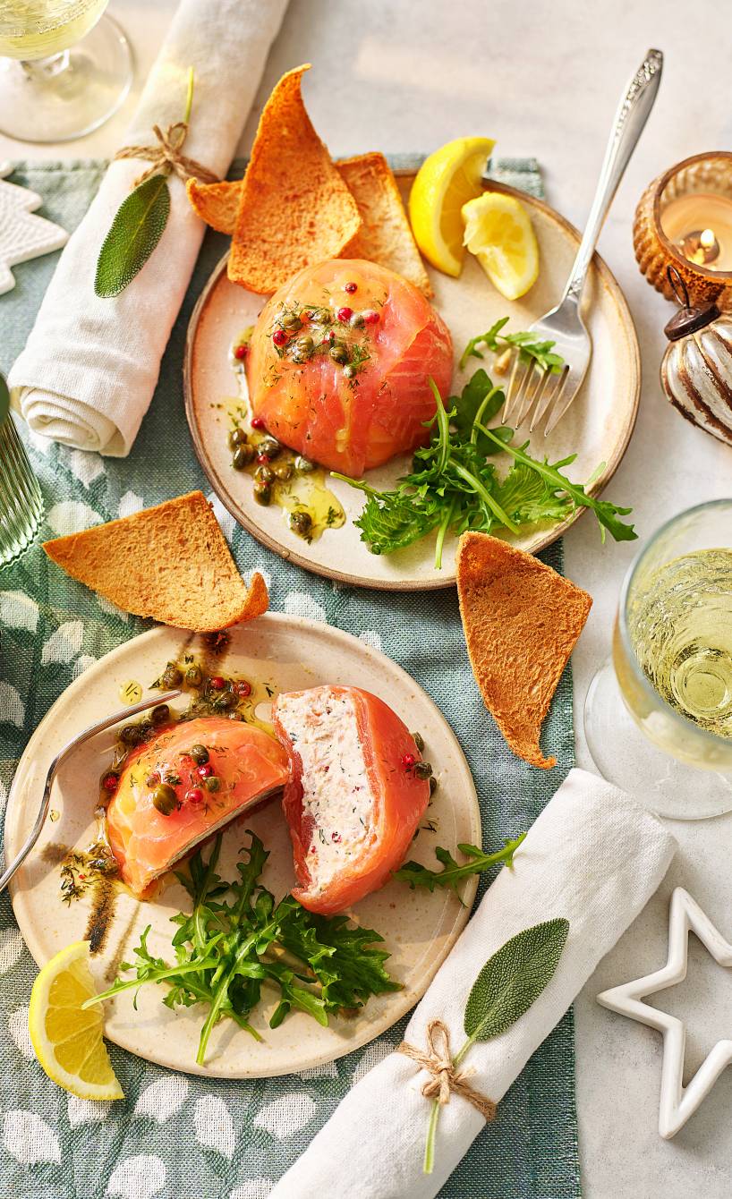 Zwei selbstgemachte  Lachsterrinen angerichtet auf Vorspeisentellern, eine halbiert und Frischkäse-Lachs-Füllung sichtbar
