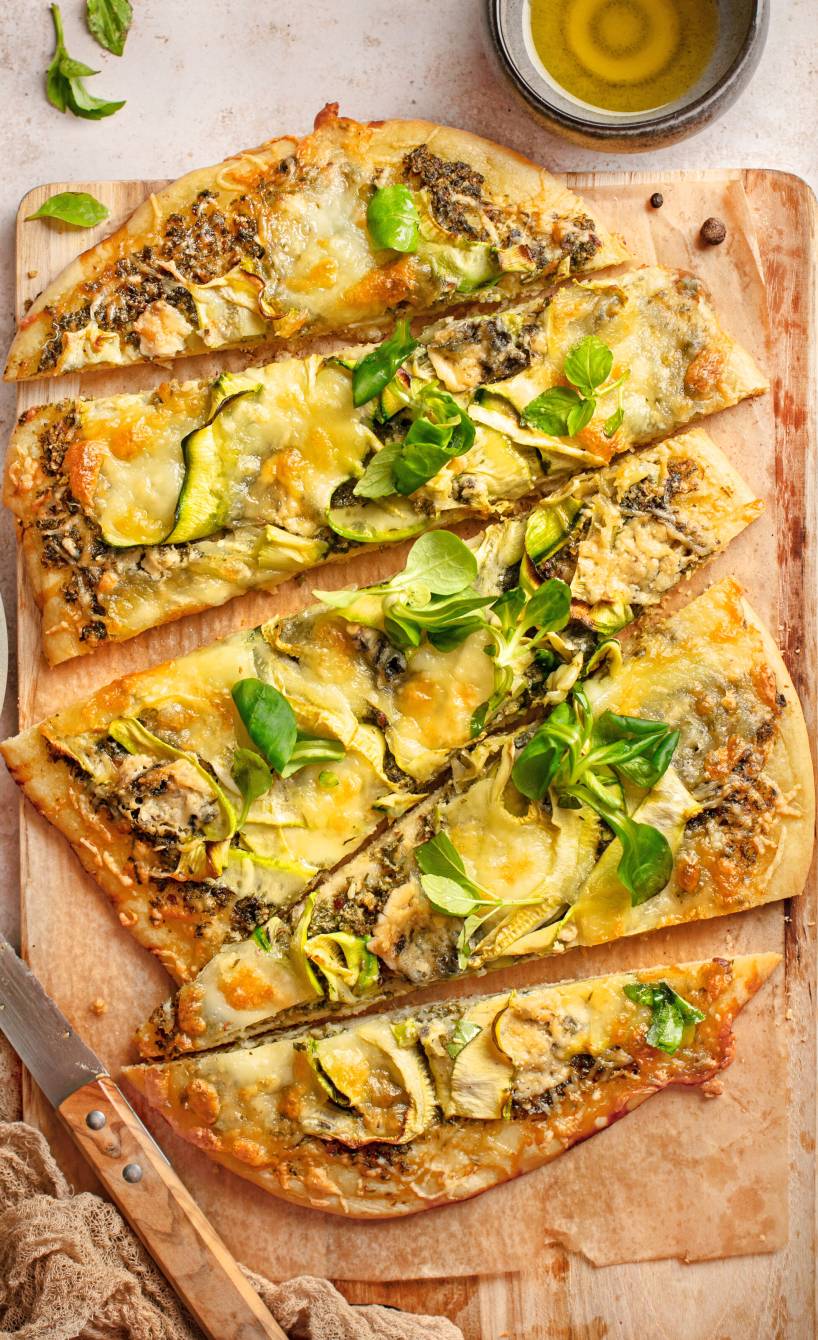 in Streifen geschnittener Flammkuchen mit Feldsalat-Pesto und Zucchini Belag auf einem Holzbrett