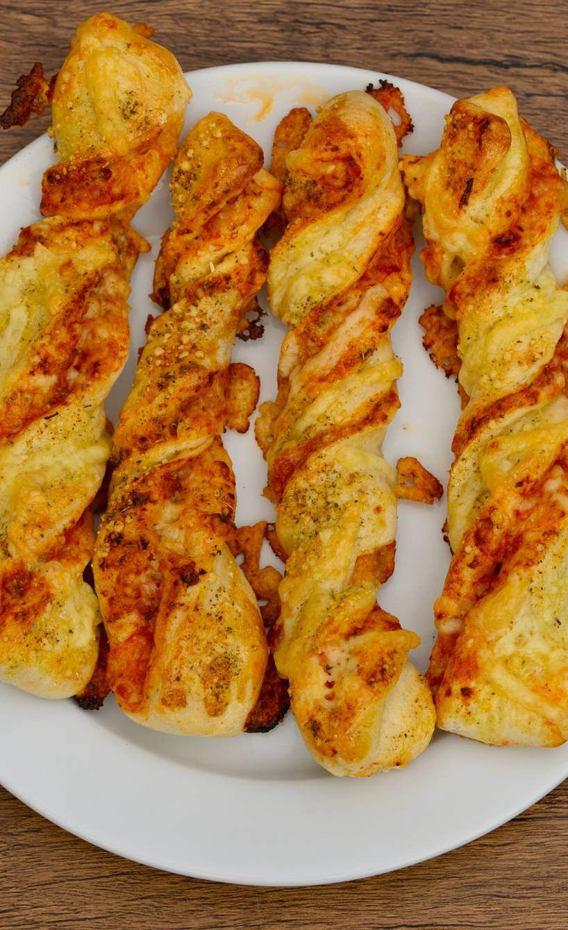 Vier selbst gebackene, gedrehte Pizzastangen angerichtet auf einem Teller