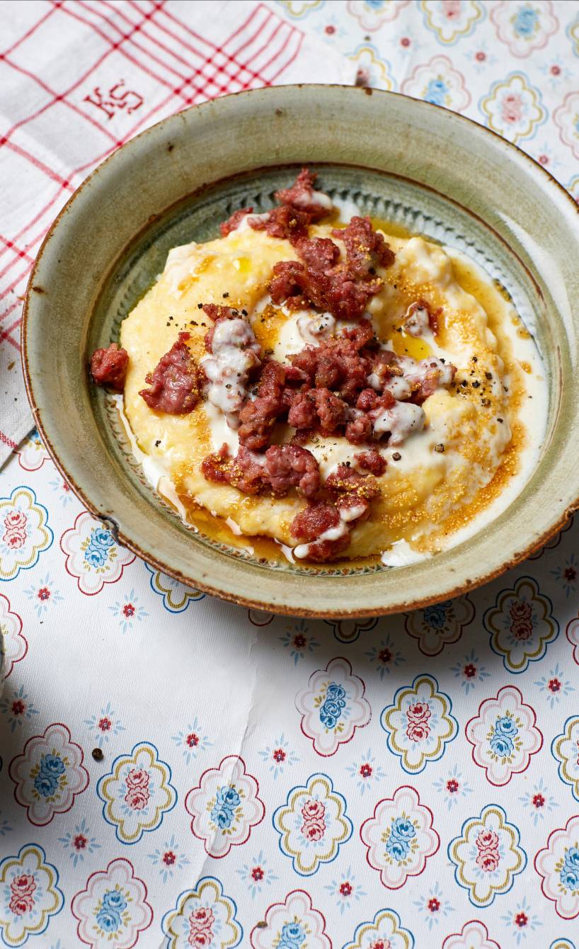 Polenta getoppt mit gebratener Salsiccia und Käsesoße angerichtet auf einem tiefen Teller
