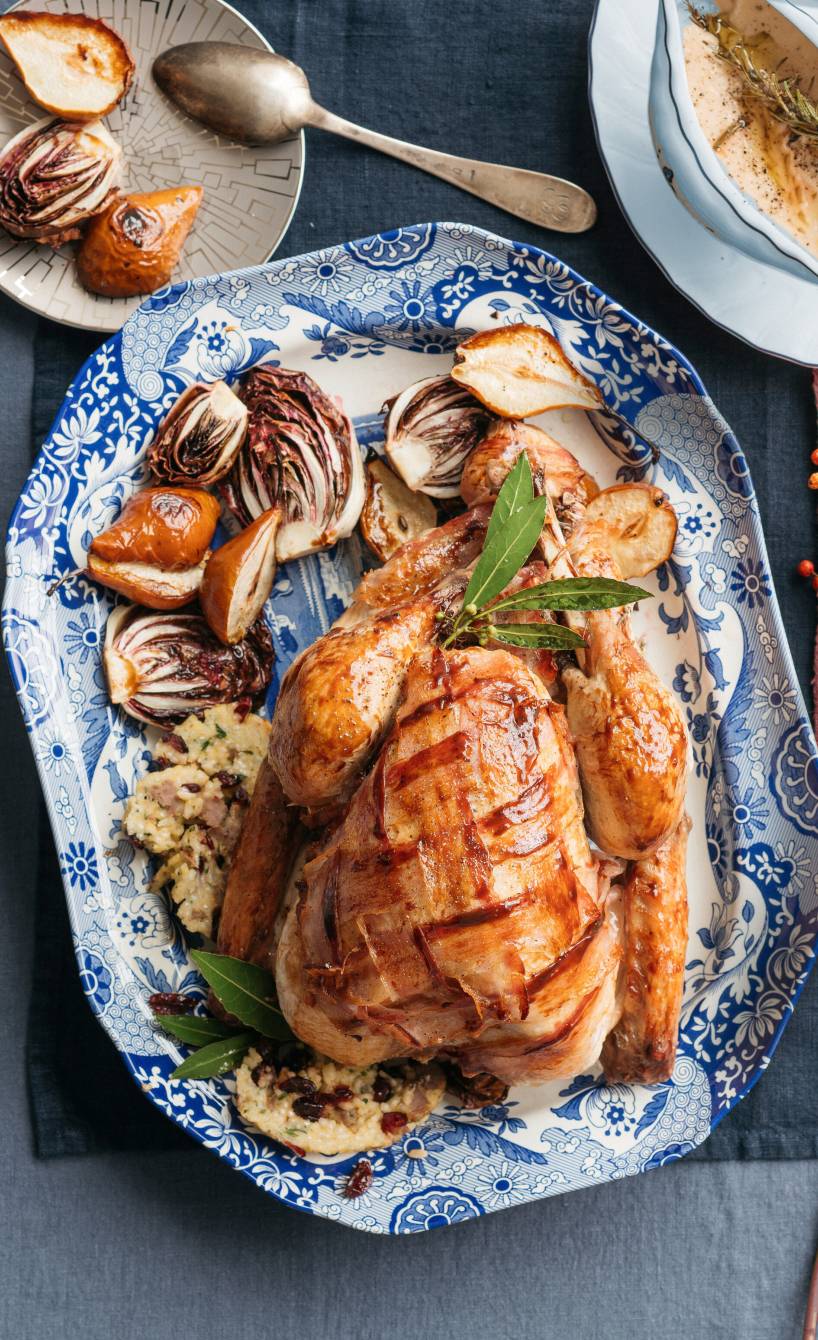 GanzePoulard mit Salsiccia-Reis-Füllung gebettet auf Radicchio-Birnen-Gemüse auf einer Servierplatte, daneben eine Sauciere mit Soße