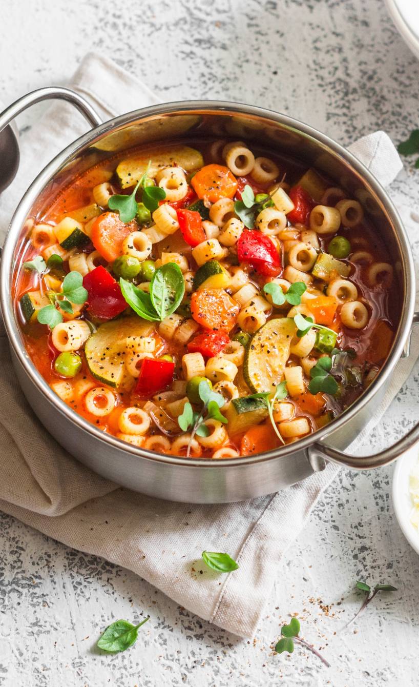 Selbstgekochte italienische Minestrone in einem Topf auf einem Tisch, daneben geröstete Ciabatta und Olivenöl